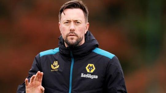 Ian Burchnall in a Wolves training top raises his right hand