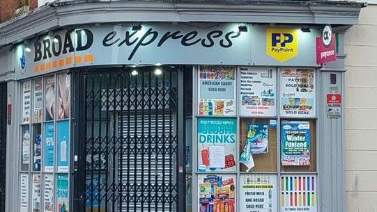 Broad Express shop has a light blue sign above a black gated doorway.