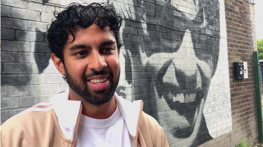 Oasis fan Raz Ashraf smiles by a mural in Burnage of the Gallagher brothers