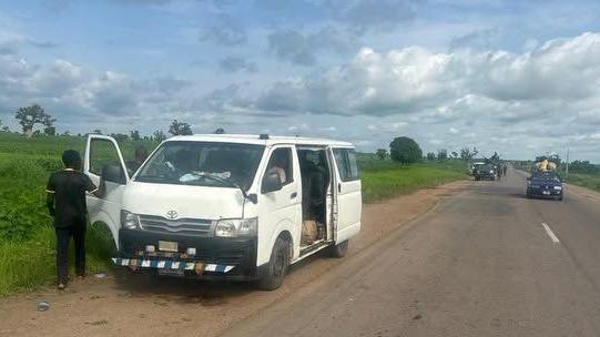 A man stands next to a white van with its doors open on the side of a Nigerian road in Tsafe, Zamfara state