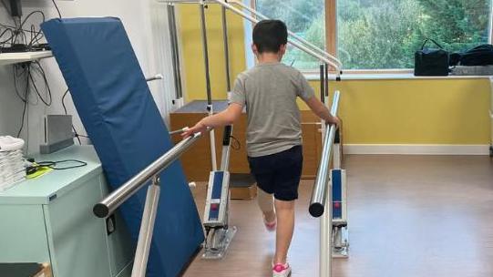 Harry is seen walking on a rehabilitation parallel bar setup as part of his physio therapy.