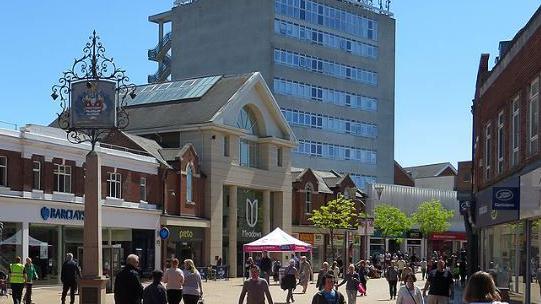 Chelmsford High Street in the sun with a range of shops and lots of people, with an office block in the background.