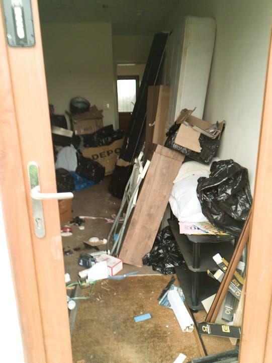 A door into a house shows rubbish, cardboard boxes and black bags scattered on the floor