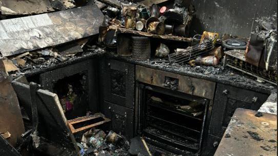 The charred kitchen. The stove and utensils can be seen in the ashes.