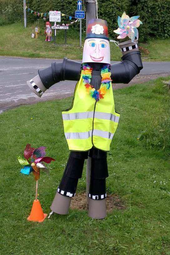 A model of a police officer made from plant pots standing on grass next to a road.