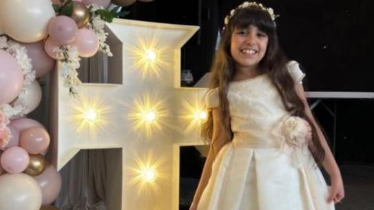 Alice da Silva Aguiar smiles at the camera wearing her white Communion dress