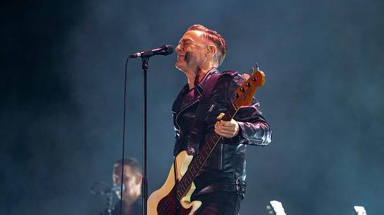 Canadian singer Bryan Adams wearing a black leather jacket and black pants is holding a guitar in his hand and in front is a mic stand during his performance at NESCO Centre, Goregaon on December 13, 2024 in Mumbai, India.