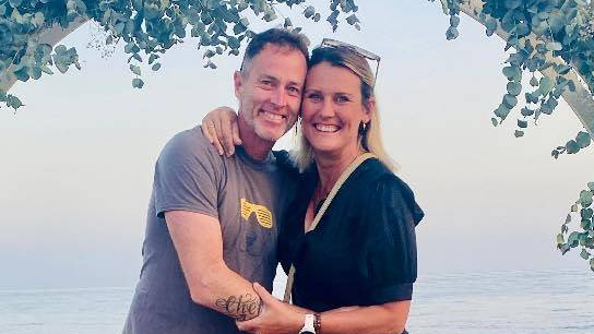 A husband and wife on holiday. They are smiling and look happy.