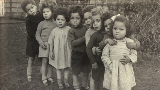 A black and white photograph of a line of eight children looking at the camera