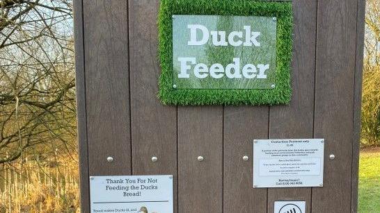 Wooden vending unit with green sign saying Duck feeder and another sign saying Thank you for not feeding the ducks bread.