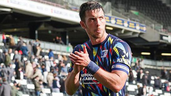 Niall Canavan, in Barrow's multi-coloured shirt, applauds fans as he leaves the field.