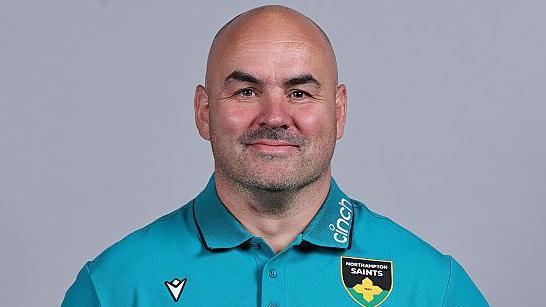 Jim Henry posing at a photoshoot in a bright blue Northampton Saints polo shirt.
