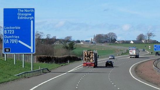 Three-lane motorway with large blue sign indicating roads to Lockerbie and Dumfries