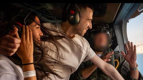 A young couple pictured looking out of an open helicopter door during a flight.