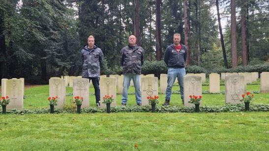 Brothers Kevin, Ron and Pim Klunder standing in front of the graves of service people who died during World War Two 