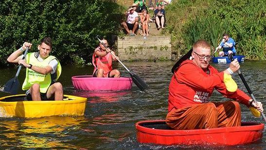 Three men in yellow, pink and red with matching coracle boats paddle in the River Severn during a race