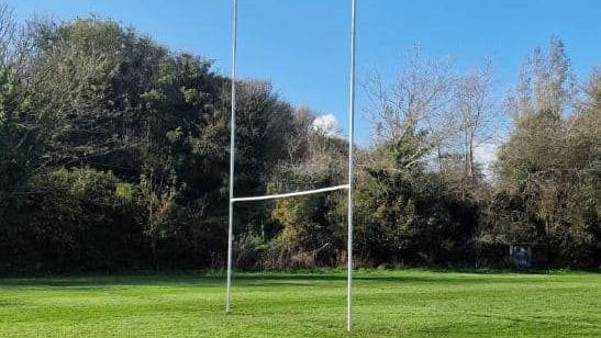 A set of rugby posts at a Cornish rugby club's ground on a sunny day with trees surrounding the playing field.