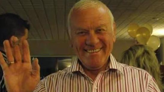 Frank Knight has white hair and a white shirt with coloured stripes