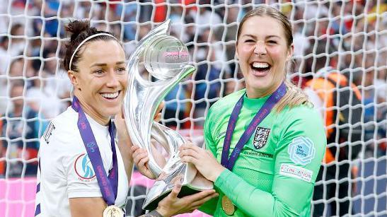Lucy Bronze y Mary Earps sostienen el trofeo de la Eurocopa 2022.
