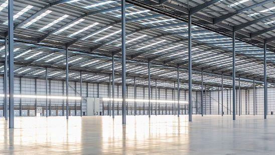 The inside of a warehouse, showing metal pillars and roof structure, grey walls and shiny floor