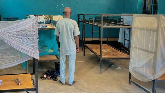 A man stands with his back to the camera in a dormitory with beds at St Mary's boarding school in Papiri village in Niger state.