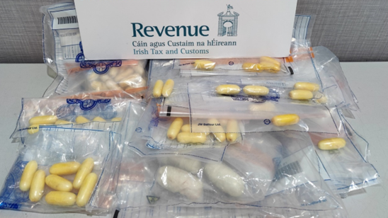 Pellets of drugs inside clear plastic bags being displayed along with a sign displaying the logo of the Irish Revenue Service.