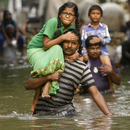 People carry children on their shoulders and wade through flood waters in Chennai, India, Thursday, Dec. 3, 2015.