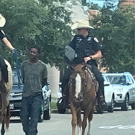 Two officers on horseback leading suspect on foot