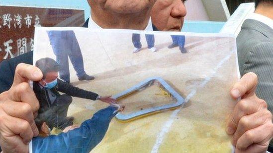 Okinawa Governor Takeshi Onaga shows a picture of the window that fell from the helicopter