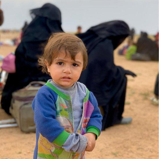 A small child with women visible behind him