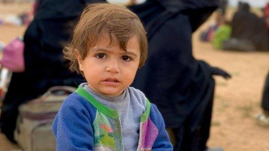 A small child with women visible behind him