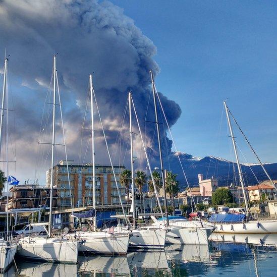 Smoke billows from volcano with yachts visible