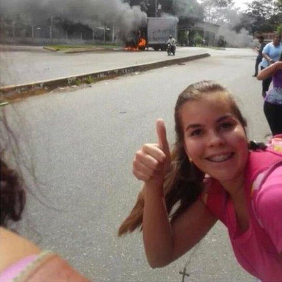 A girl is pictured doing a thumbs-up in front of a burning lorry.