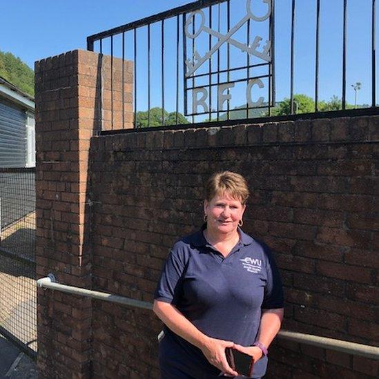 Cross Keys Rugby Club secretary Angie Prangell standing beneath a club sign