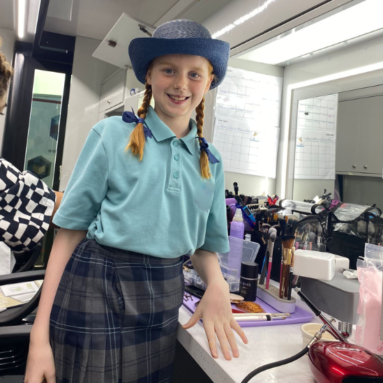 Anna, smiling at the camera wearing a blue wide-brim hat and ribbons in her hair.