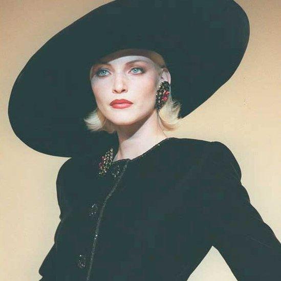 A model in large black hat, tilted to side and velvet black dress in July 1995