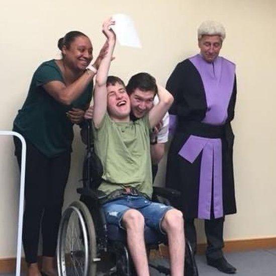 Adrian holding up his adoption paperwork with his parents