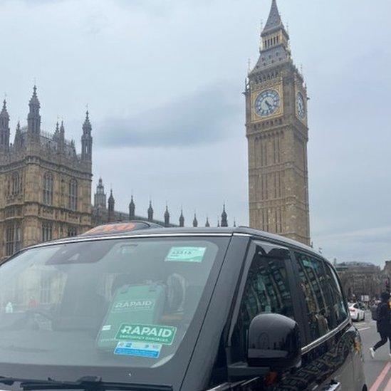 A black cab carrying Rapaid bandages and a sticker parked in front of the Palace of Westminster.