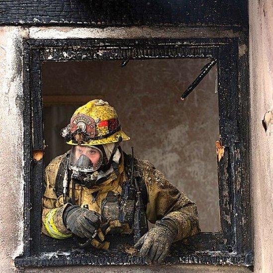 a firefighter leans out of a burnt door frame