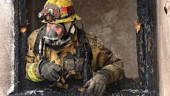 a firefighter leans out of a burnt door frame