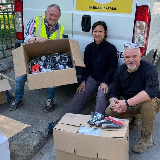 Kev Draper (left) with two other volunteer helpers sitting with cardboard boxes with equipment in front of a van