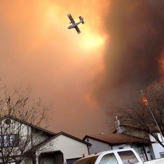 Smoke fills the air as a small plane flies overhead in Fort McMurray, Alberta