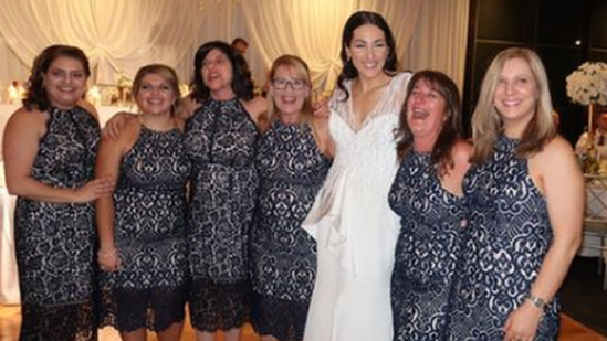 Six wedding guests in identical dresses pose for a photograph with the bride