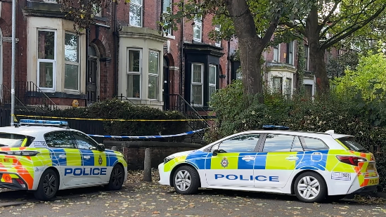 Two police cars parked outside a house, with police tape sealing off the front of the terraced houses