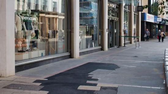 Temporary tarmac paving repairs to a stone paved pavement in Cheltenham, outside the John Lewis store