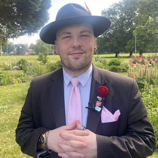 Kyle Eldridge seen wearing his trilby, two-piece suit, shirt and tie, along with a pierced left ear and a ring on his left thumb