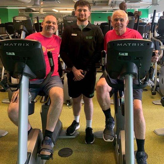 Darryl Claypole undertaking his virtual cycle ride with support from Tom and a personal trainer