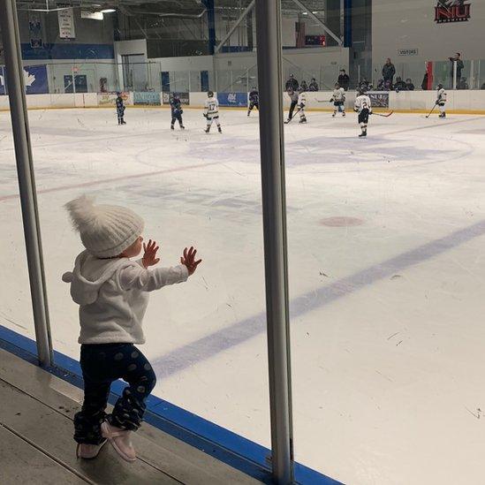 Chloe seen leaning against a window at a hockey game