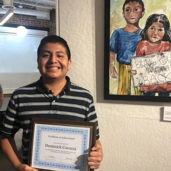 Dominick accepting a certificate of Achievement next to his winning painting