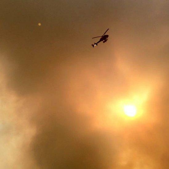 Smoke fills the air as a helicopter flies overhead in Fort McMurray, Alberta